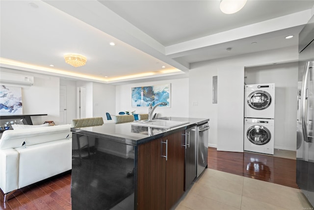 kitchen featuring stacked washer and clothes dryer, a center island with sink, sink, a tray ceiling, and dark brown cabinets