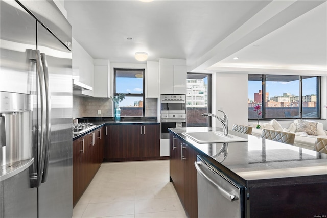 kitchen featuring backsplash, white cabinets, a center island with sink, sink, and appliances with stainless steel finishes