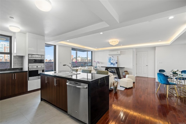 kitchen featuring a kitchen island with sink, sink, dark brown cabinets, white cabinetry, and stainless steel appliances