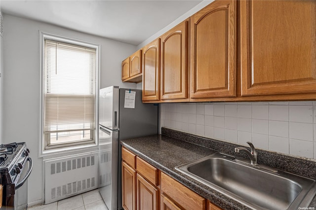 kitchen with backsplash, radiator, sink, light tile patterned floors, and appliances with stainless steel finishes