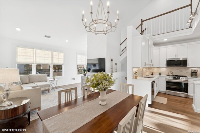 dining area featuring an inviting chandelier, sink, high vaulted ceiling, and light hardwood / wood-style flooring