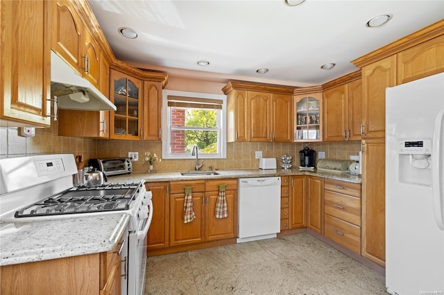 kitchen with backsplash, light stone counters, sink, and white appliances