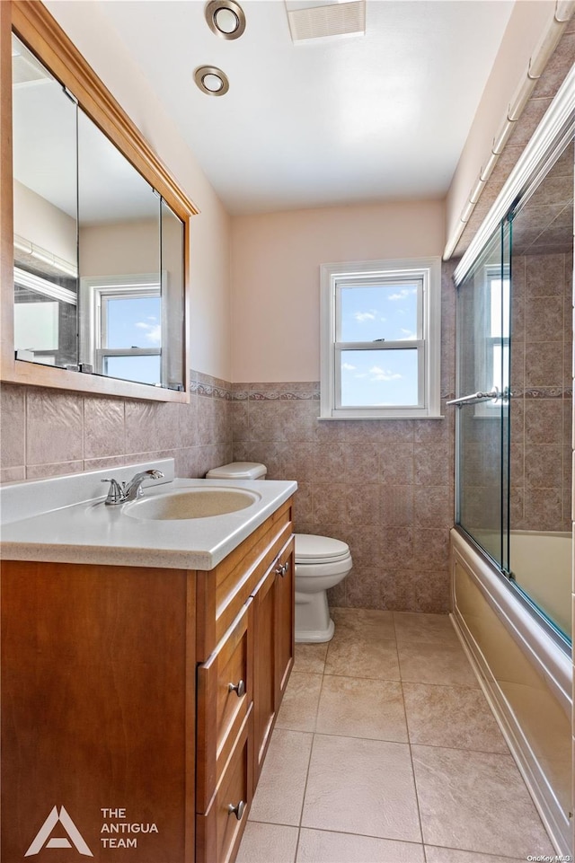 full bathroom featuring tile patterned flooring, combined bath / shower with glass door, toilet, vanity, and tile walls