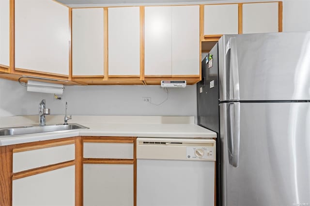 kitchen with white dishwasher, stainless steel refrigerator, white cabinetry, and sink