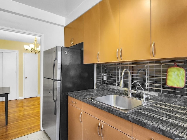 kitchen with light wood-type flooring, backsplash, sink, a chandelier, and stainless steel refrigerator