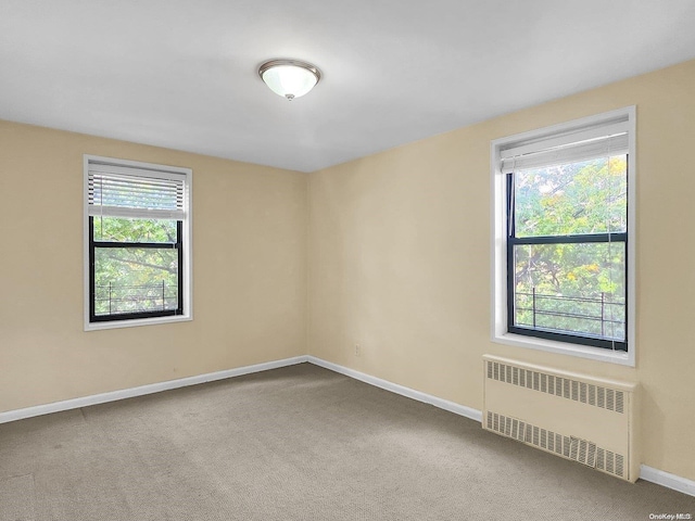 carpeted empty room featuring radiator heating unit and plenty of natural light