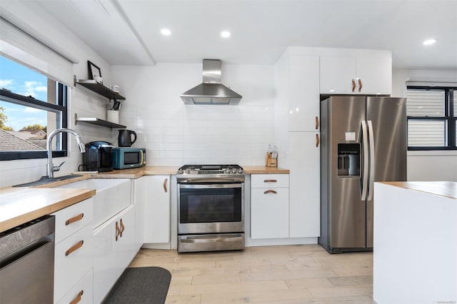 kitchen with stainless steel appliances, white cabinetry, wall chimney exhaust hood, and light hardwood / wood-style floors