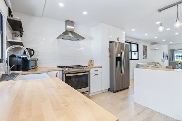 kitchen with wood counters, wall chimney range hood, stainless steel appliances, and hanging light fixtures