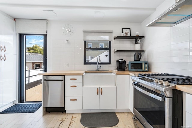 kitchen with white cabinetry, sink, light hardwood / wood-style floors, exhaust hood, and appliances with stainless steel finishes