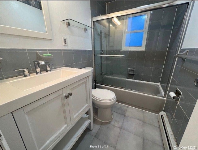 full bathroom with tile patterned flooring, a baseboard heating unit, combined bath / shower with glass door, vanity, and tile walls