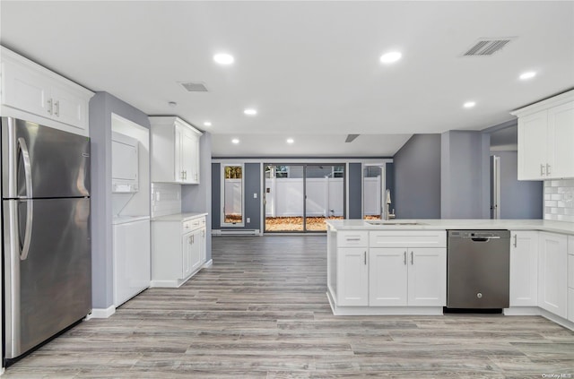 kitchen with white cabinetry, sink, stacked washing maching and dryer, stainless steel appliances, and light hardwood / wood-style floors