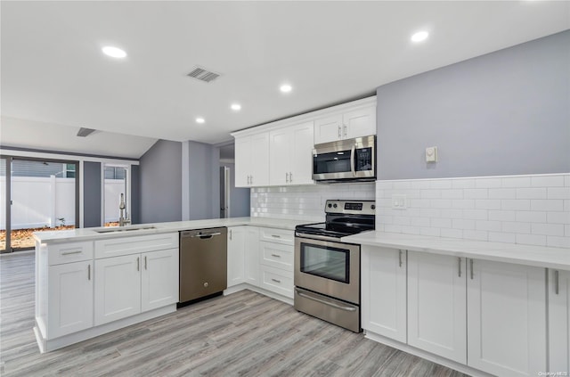 kitchen featuring kitchen peninsula, appliances with stainless steel finishes, sink, light hardwood / wood-style flooring, and white cabinetry