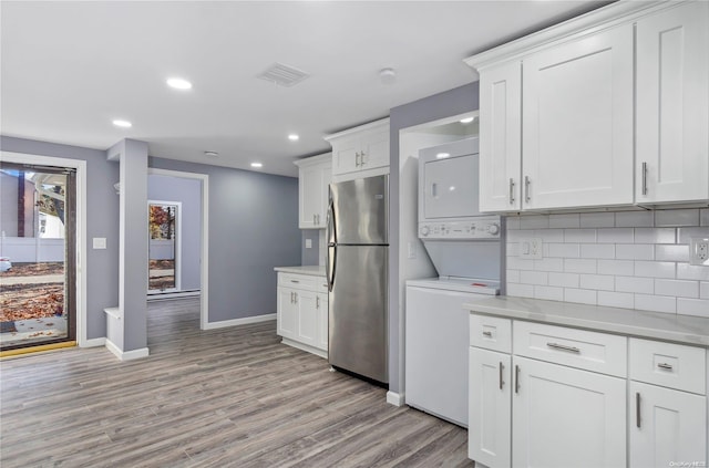 kitchen with white cabinets, light hardwood / wood-style flooring, tasteful backsplash, stacked washer / dryer, and stainless steel refrigerator