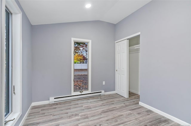 unfurnished bedroom featuring vaulted ceiling, light hardwood / wood-style flooring, a closet, and a baseboard heating unit