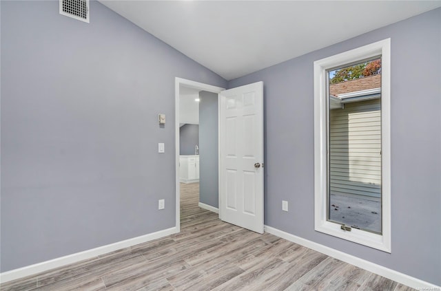 empty room with light hardwood / wood-style floors and vaulted ceiling