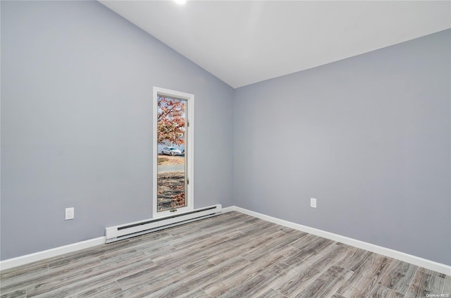 spare room featuring baseboard heating, light hardwood / wood-style flooring, and vaulted ceiling