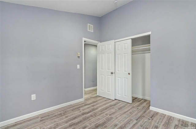 unfurnished bedroom with light hardwood / wood-style floors, a high ceiling, and a closet