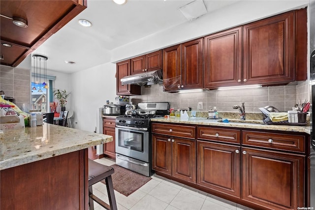 kitchen featuring sink, hanging light fixtures, stainless steel gas range, light stone counters, and decorative backsplash