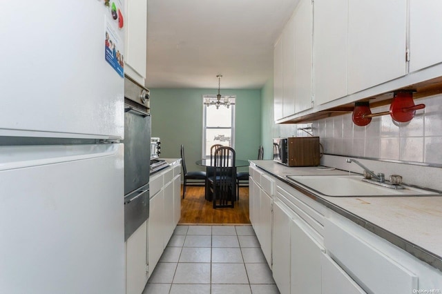 kitchen featuring sink, white refrigerator, a chandelier, white cabinetry, and hanging light fixtures