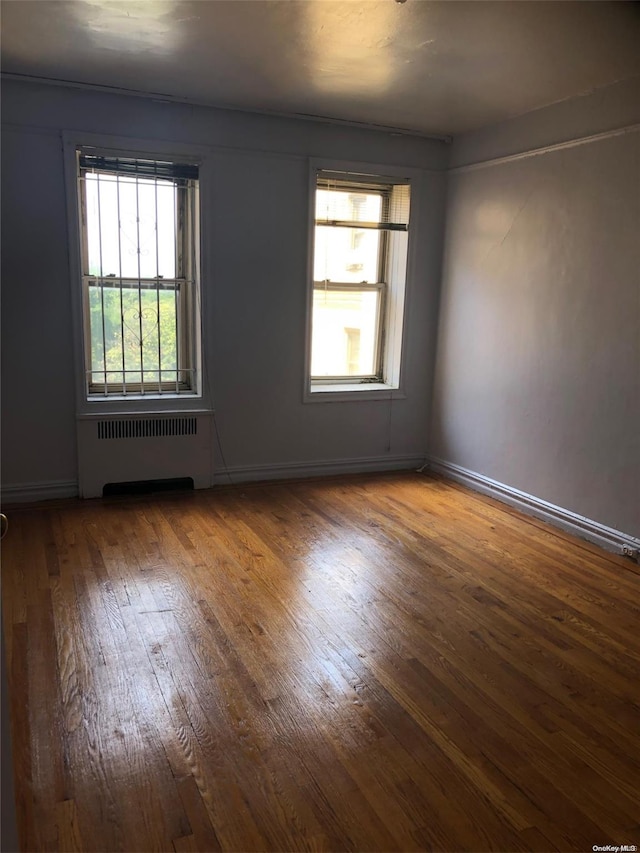 spare room featuring radiator heating unit, hardwood / wood-style flooring, and plenty of natural light