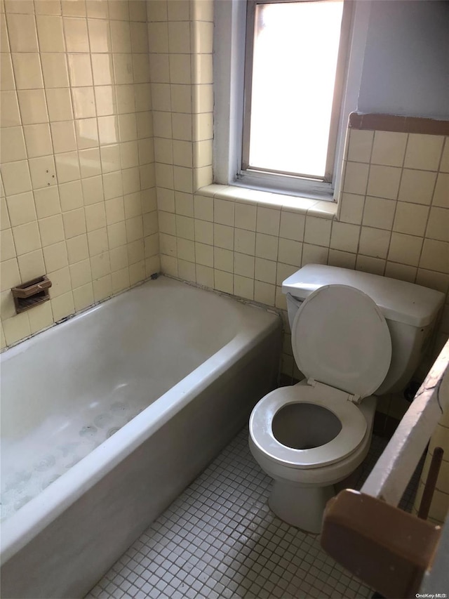 bathroom with tile patterned flooring, a bath, toilet, and tile walls