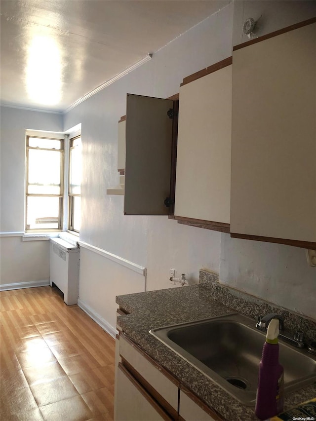 kitchen featuring radiator, sink, crown molding, white cabinets, and light wood-type flooring