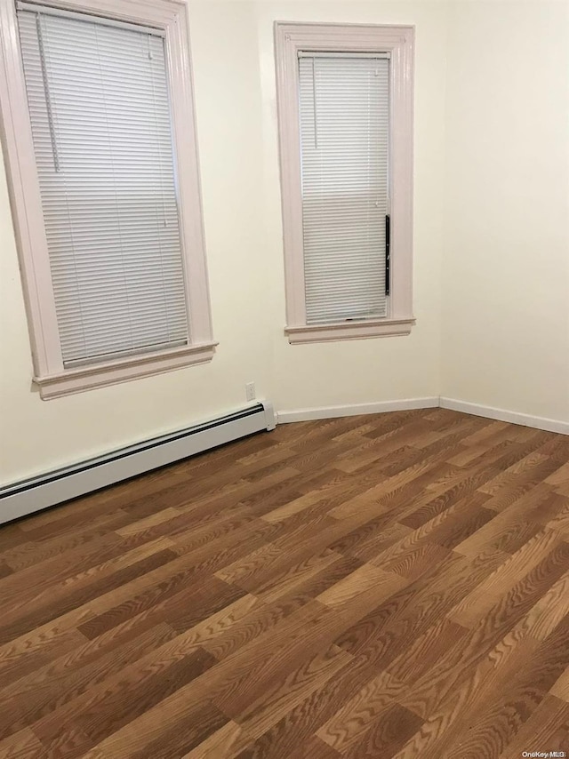 spare room featuring a baseboard heating unit and dark wood-type flooring