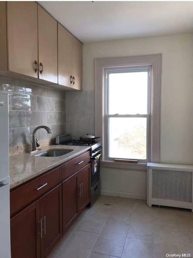 kitchen featuring backsplash, light stone counters, radiator, high end stainless steel range oven, and sink