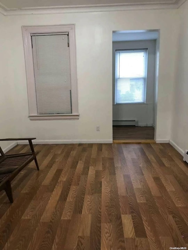 empty room with dark hardwood / wood-style flooring, ornamental molding, and a baseboard heating unit