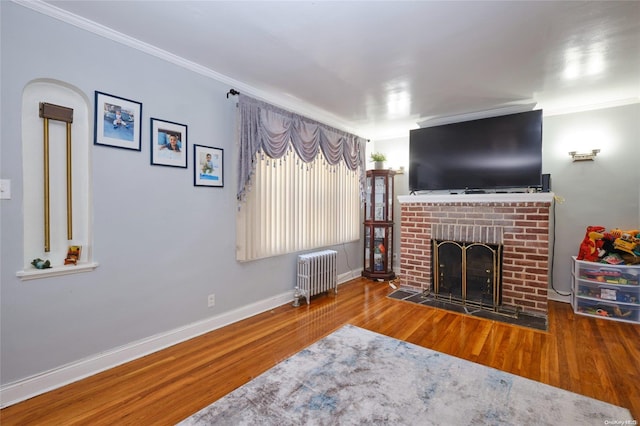 living room featuring a fireplace, hardwood / wood-style flooring, radiator, and crown molding