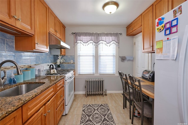 kitchen featuring white appliances, backsplash, radiator, sink, and stone countertops