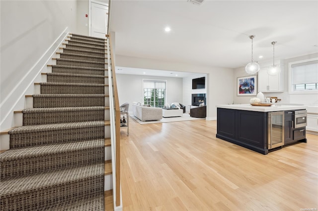 kitchen with light hardwood / wood-style floors, decorative light fixtures, a large fireplace, white cabinetry, and beverage cooler