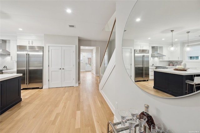 kitchen featuring light hardwood / wood-style floors, white cabinetry, stainless steel built in refrigerator, and wall chimney range hood