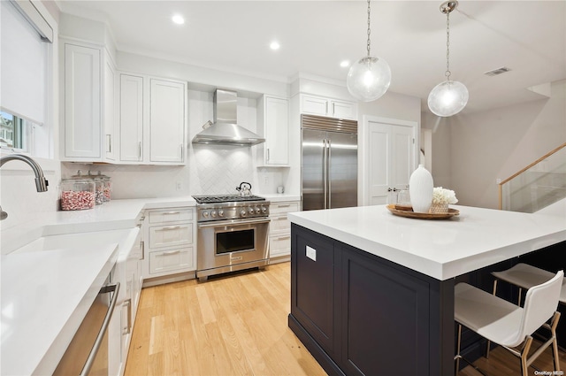 kitchen featuring high quality appliances, white cabinets, and wall chimney exhaust hood