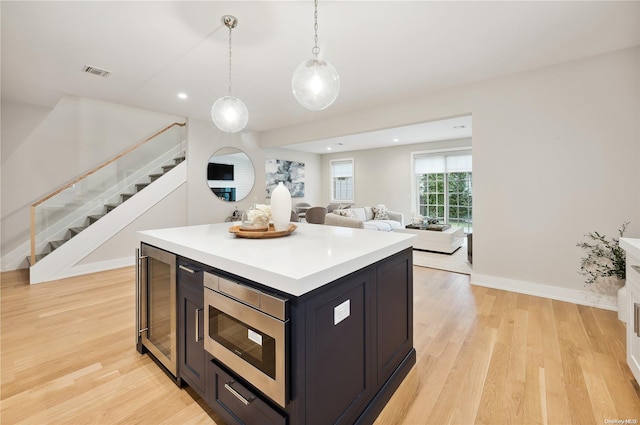 kitchen with stainless steel microwave, a center island, hanging light fixtures, wine cooler, and light hardwood / wood-style flooring