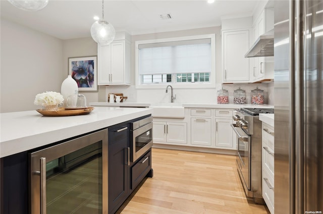 kitchen with pendant lighting, white cabinets, appliances with stainless steel finishes, light hardwood / wood-style floors, and beverage cooler