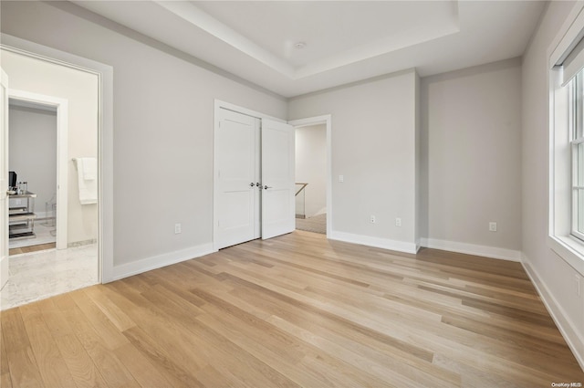 unfurnished bedroom featuring a raised ceiling, multiple windows, ensuite bath, and light hardwood / wood-style floors