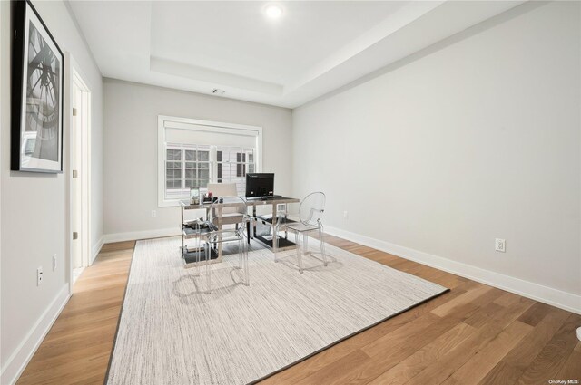 office space with a tray ceiling and wood-type flooring