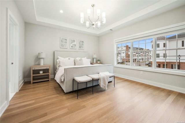 bedroom with a notable chandelier, a raised ceiling, and light hardwood / wood-style flooring