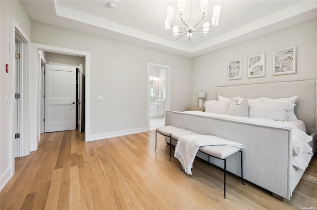 bedroom with a raised ceiling, connected bathroom, a chandelier, and wood-type flooring