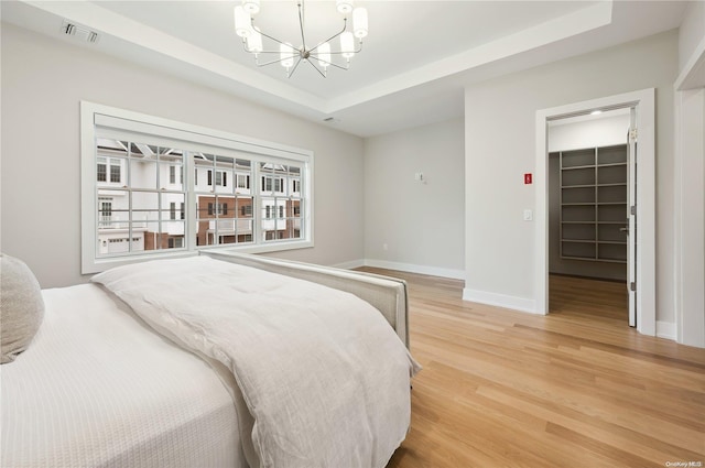 bedroom featuring hardwood / wood-style floors, a closet, a walk in closet, a tray ceiling, and a chandelier