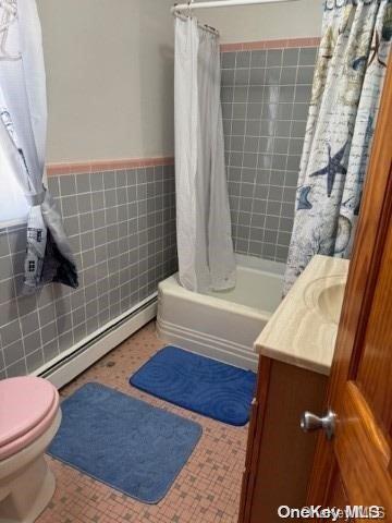 full bathroom featuring vanity, shower / bath combo with shower curtain, a baseboard heating unit, tile walls, and toilet