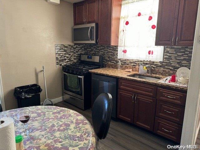 kitchen featuring light stone countertops, sink, dark wood-type flooring, stainless steel appliances, and backsplash