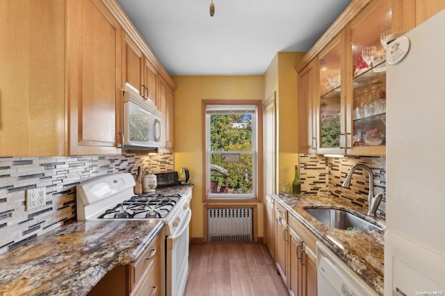 kitchen with radiator, sink, light hardwood / wood-style floors, stone countertops, and white appliances