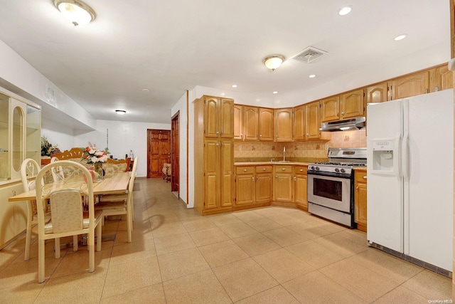 kitchen with tasteful backsplash, white refrigerator with ice dispenser, sink, and gas range