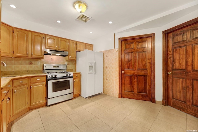 kitchen featuring decorative backsplash, sink, gas range oven, and white refrigerator with ice dispenser