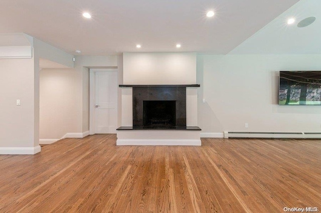 unfurnished living room featuring a tile fireplace, a baseboard radiator, and light hardwood / wood-style flooring