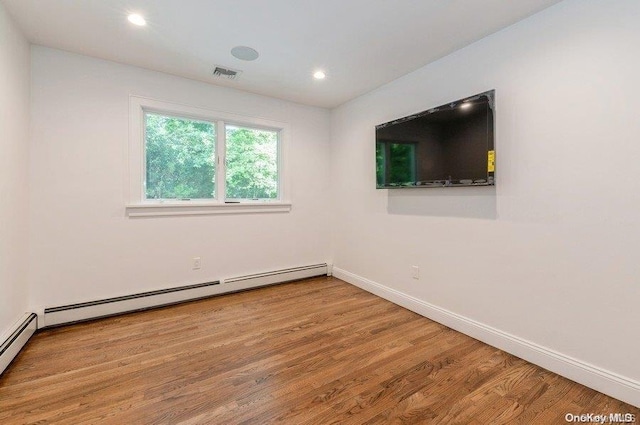 empty room featuring wood-type flooring and a baseboard heating unit