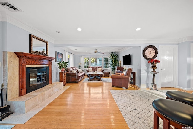 living room with light hardwood / wood-style flooring, ceiling fan, ornamental molding, and a tiled fireplace