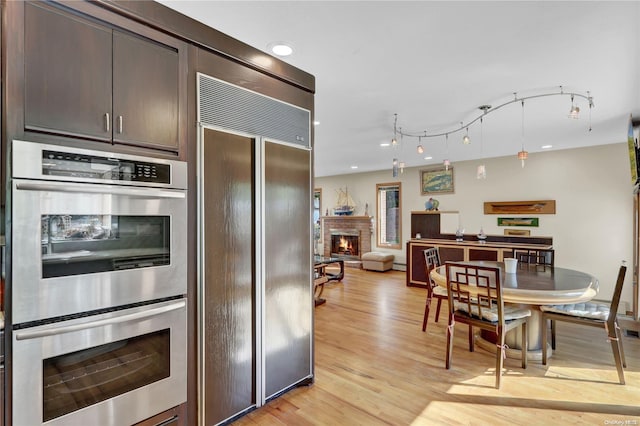 kitchen with stainless steel double oven, light hardwood / wood-style flooring, built in refrigerator, and dark brown cabinetry